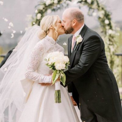 RJ Styles Co Rachel Jones - Alberta Bridal Hairstylist and Hairstyling Lessons - Blonde bride with low modern bun hairstyle kissing her groom at the end of the aisle after her wedding ceremony 2