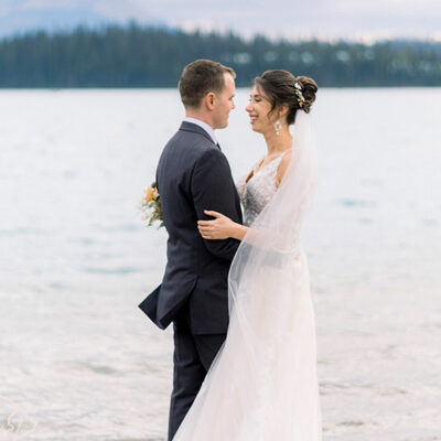 RJ Styles Co Rachel Jones - Alberta Bridal Hairstylist and Hairstyling Lessons - bride and groom looking at each other smiling in front of water romantic updo