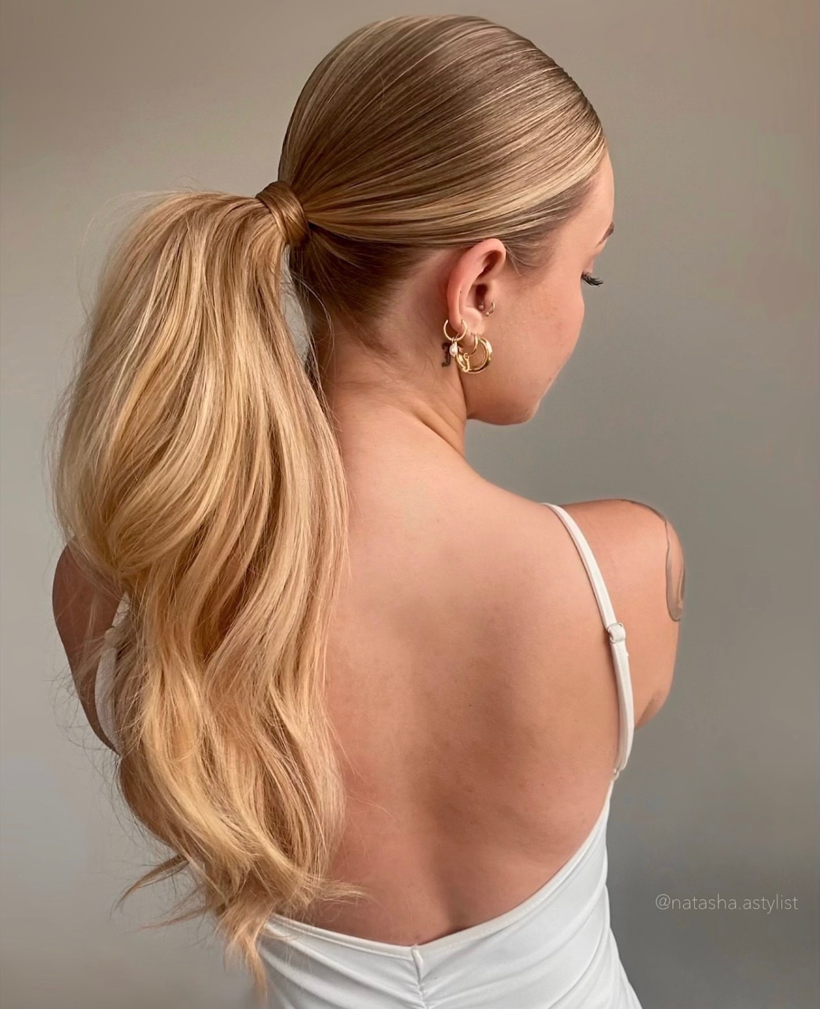 Blonde hair in a sleek yet voluminous pony tail on model with white top